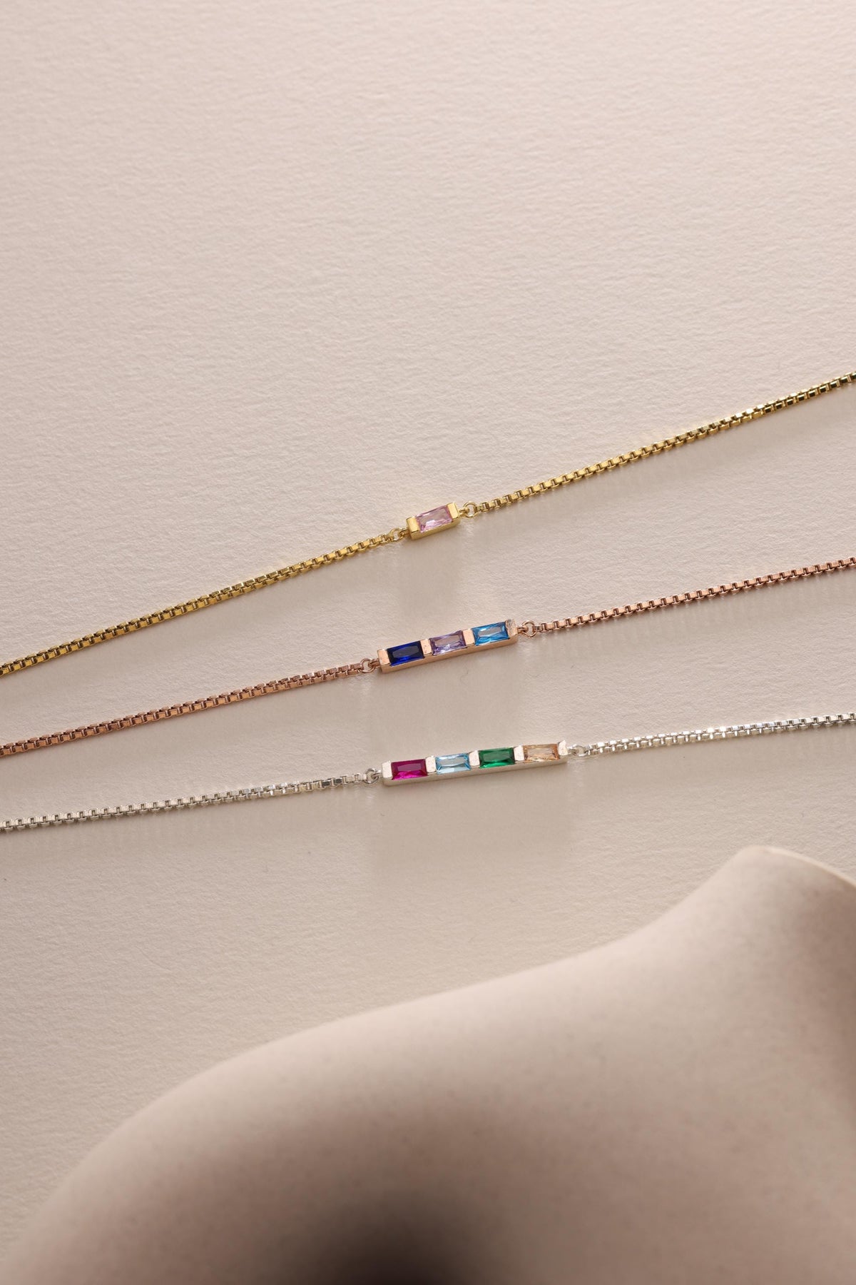 Baguette birthstone bracelets laid flat in three finishes
