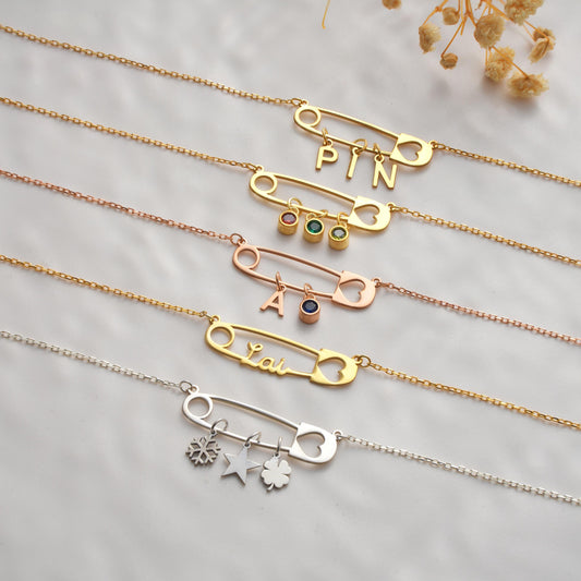 Personalized safety pin necklaces laid flat with birthstones