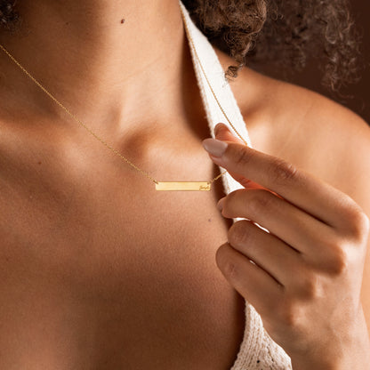 Gold personalized horizontal bar necklace held by model