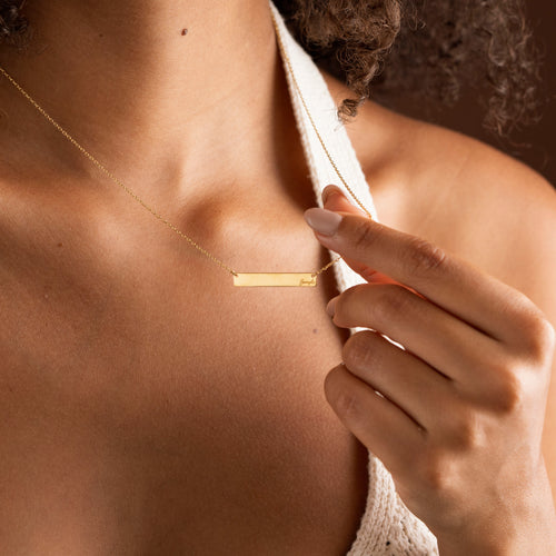 Gold personalized horizontal bar necklace held by model