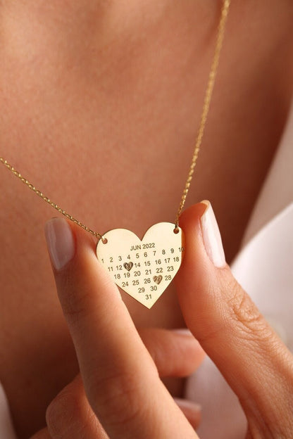 Heart calendar necklace in gold held in hand