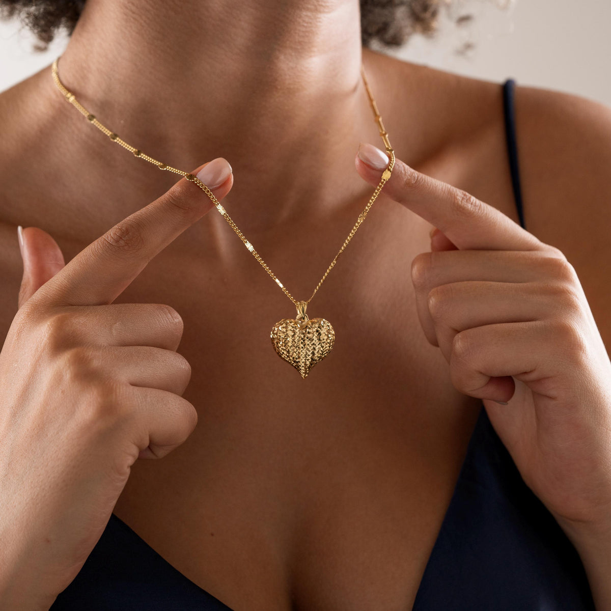 Textured heart pendant necklace held up by a woman
