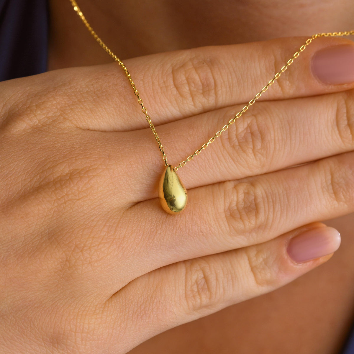 Smooth teardrop pendant necklace in gold held in hand