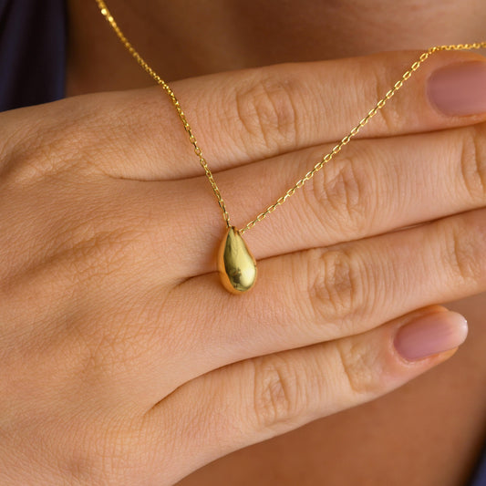 Smooth teardrop pendant necklace in gold held in hand