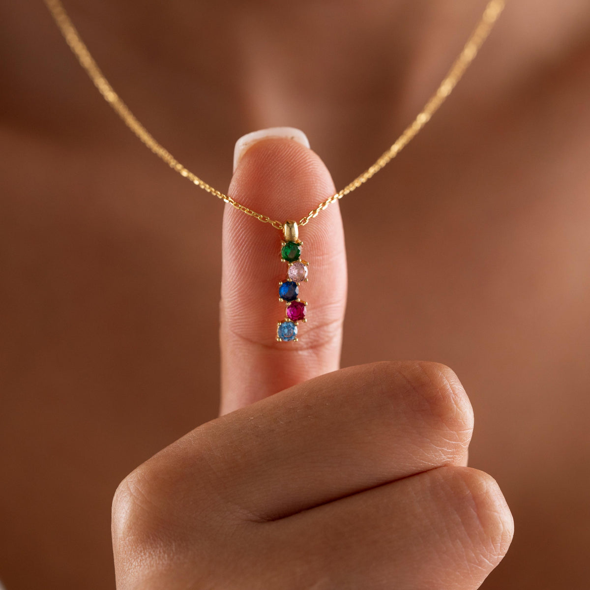 Vertical family birthstone necklace held up by a woman