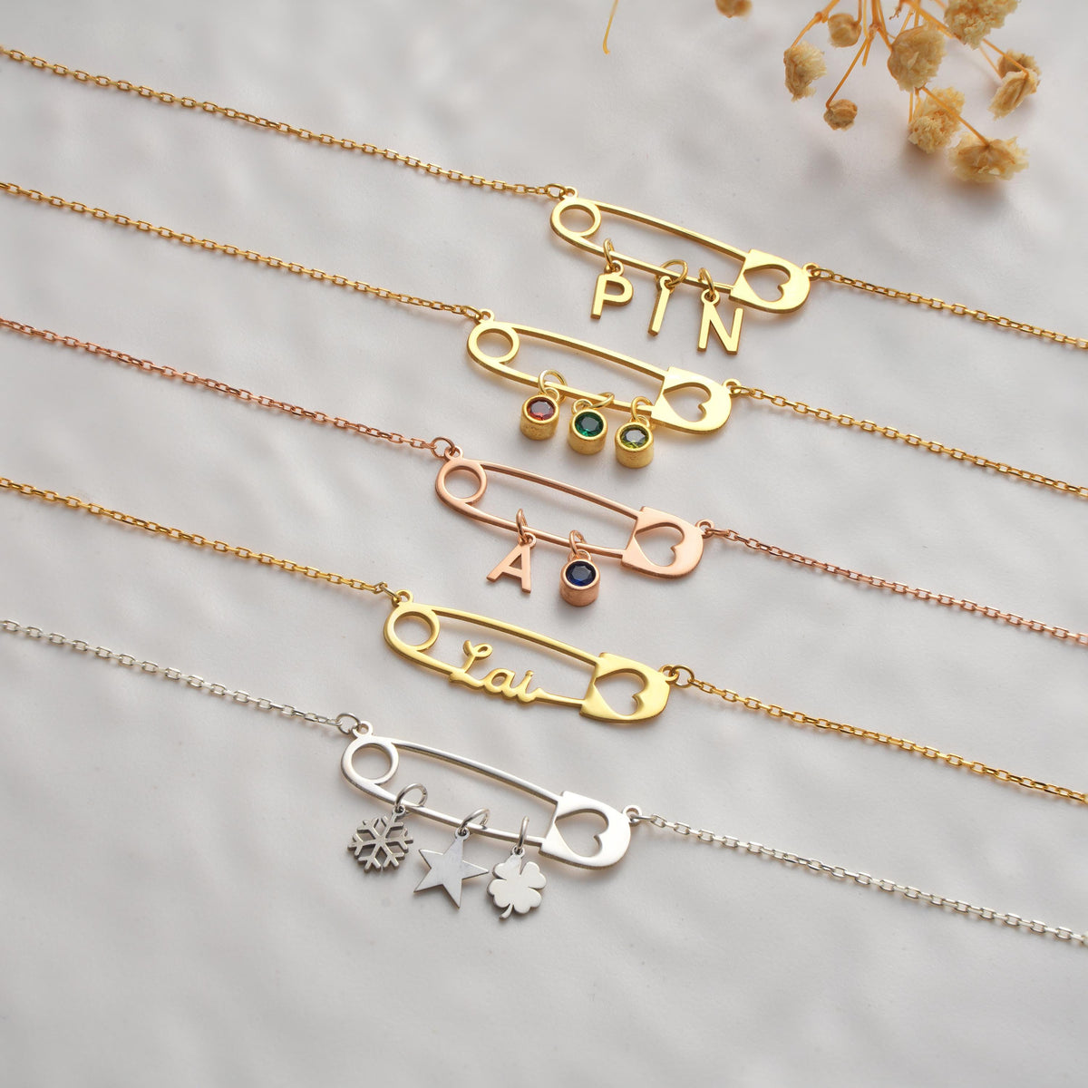 Personalized safety pin necklaces laid flat with birthstones
