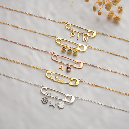 Personalized safety pin necklaces laid flat with birthstones